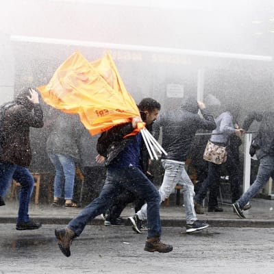 Mielenosoittajien joukko juoksee tiheässä vesisumussa  märällä kadulla. 