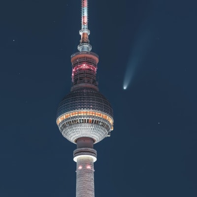 Berliinin tv-tornin huippu, taivaalla muutamia tähtiä ja pyrstöllinen komeetta. 