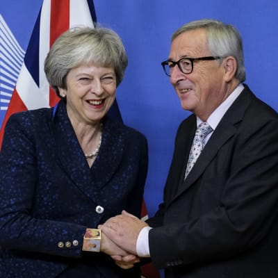 Hymyilyvä nainen ja mies kättelevät, taustalla Britannian lippuja EU-komissio merkki.