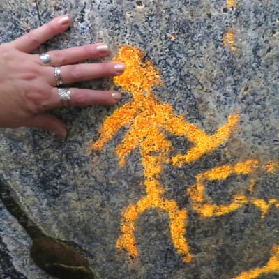 Käsi kalliomaalauksen ihmishahmoa vasten