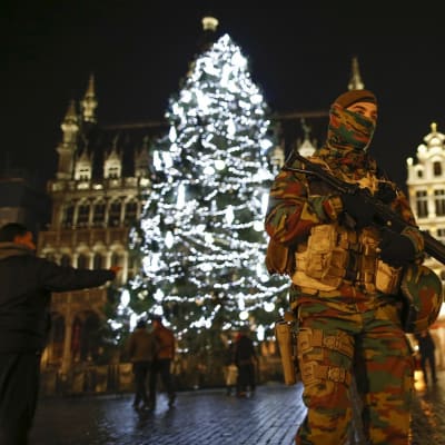 Aseistautunut maastopukuinen sotilas partioi valaistun joulukuusen edessä.