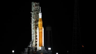 En orange och vit raket står startklar och upplyst i mörkret.