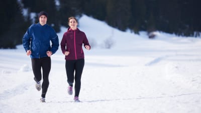 Två personer som ser glada ut, ute på en löprunda i snöigt landskap.