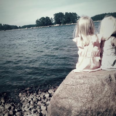 kaksi tyttöä istuu selin kameraan kivellä