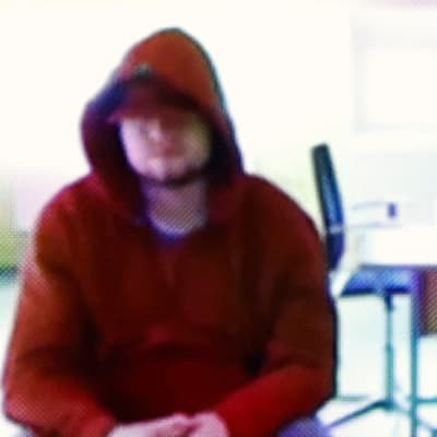 Pikselisessä kuvassa punaiseen huppariin pukeutunut mies istuu nojaten polviinsa. Kasvoja peittää myös lippalakki.