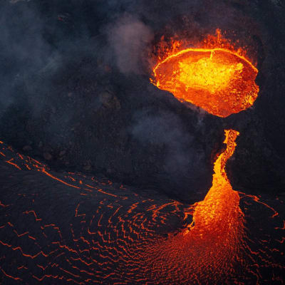Öinen näkymä tulivuoren kalderan punakeltaisena hehkuvasta laavasta, jota myös valuu rinnettä pitkin mereen, ja ilmassa leijuvasta pyroplastisesta aineesta. 