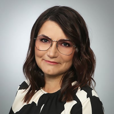 Mörkhårig kvinna med glasögon framför en grå vägg.