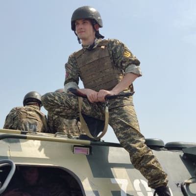 Ung ukrainsk man med vapen och klädd i militärkläder på ett militärt fordon.