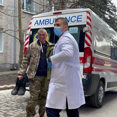 En läkare hjälper en sårad man i camouflagedräkt intill en ambulans.