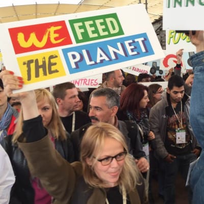 Mielenosoittaja pitelee kylttiä, jossa lukee "We Feed the Planet".