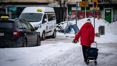 Två taxibilar står parkerade vid några butiker. En äldre person går förbi.