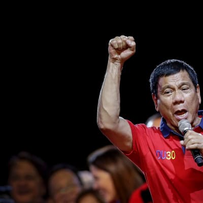 Duterte puhuu vasemmassa kädessään olevaan mikrofoniin ja pitää oikeaa kättään nyrkissä.