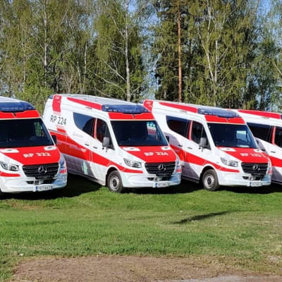 Neljä Pohjanmaan hyvinvointialueen uutta punavalkoista ambulanssia on pysäköity riviin nurmikolle.