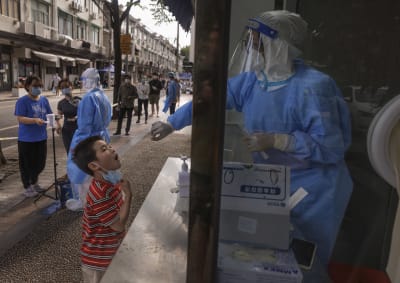 suojapukuun pukeutunut testaaja kopissa ottaa ikkunan takaa koronatestin lapsen nielusta Shanghaissa