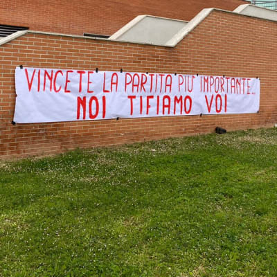 En tegelbyggnad med en banderoll där det står "Vinn den viktigast matchen, vi hejar på er" på italienska.