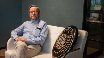 Estlands Helsingforsambassadör Harri Tiidi sitter i en soffa med ambassadens skylt bredvid sig.