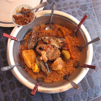 Tallrik med flera skedar dränkta i den traditionella senegalesiska maträtten Thieboudienne eller ceebu jen, som består av fisk, ris och tomatsås.
