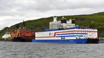 Den ryska kärnkraftsdrivna båten ligger vid hamnen. Båten är väldigt kubisk till sin design och är vit med blåa och röda streck.