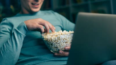 Man tittar på film på laptop och äter popcorn
