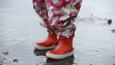 Barn i regnkläder står i vattenpöl