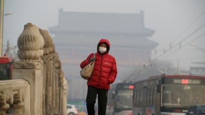 En kvinna går över en bro i Peking iklädd en ansiktsmask på grund av den förorenade luften.