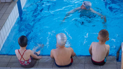 Tre barn och en simlärare i en simbassäng.