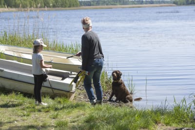En kvinna, en flicka och en hund står på en strand. Kvinnan står i beredskap för att kasta en pinne som hunden kan hämta.
