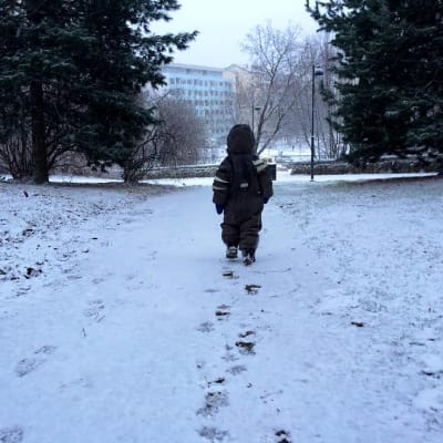 Lapsi kävelee uudella lumella kävelyväylää puistossa.