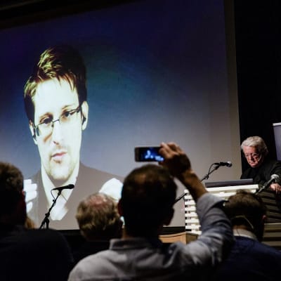 Edward Snowdenin kuva heijastettuna valkokankaalle. Yleisöt kuvaa kännyköillä.