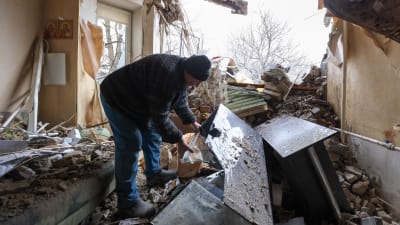 En man rotar genom bråte i en sönderbombad lägenhet.