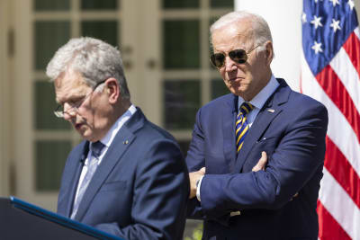 Joe Biden i förgrunden som håller armarna i kors. Han har på sig en kostym och pilotsolglasögon. I bakgrunden Sauli Niinistö i kostym vid ett talarpodium.