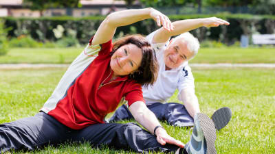 Ett äldre par gymnastiserar i en park. 