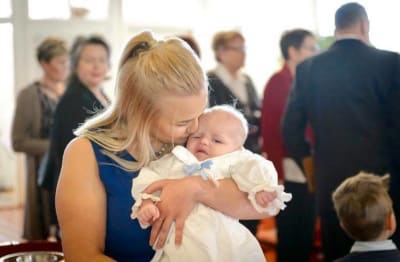 Mamma med sitt barn i famnen på ett dop. 