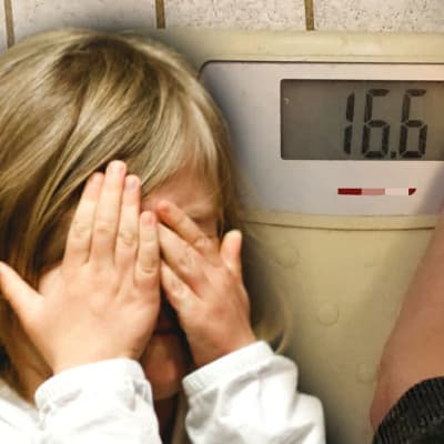 Ett barn håller för ögonen, i bakgrunden en våg som visar 16.6 kg