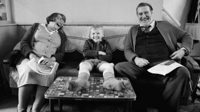 En liten pojke sitter skrattande mellan sin farmor och farfar som också skrattar.