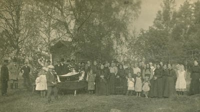 En bild tagen mellan 1910-1929. Anhöriga och vänner tar avsked av den avlidne på gården innan kistans lock sätts på.