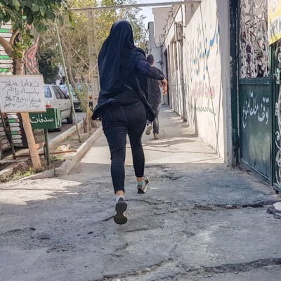 Kvinna med huvudduk rusar iväg efter sammandrabbningar med polisen i Teheran.
