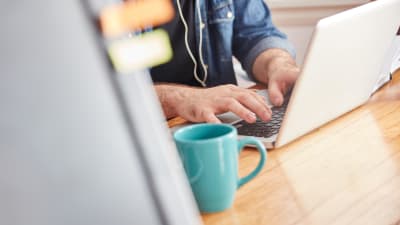 En man som skriver på en laptop. Bredvid honom står en kaffekopp. 