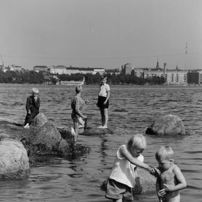 Mustavalkokuva lapsista leikkimässä rannalla 1960-luvulla.