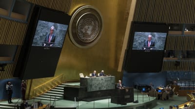 Antonio Guterres håller tal i FN:s stora sal. Han syns i talarstolen och i närbild på två stora skärmar på ömse sidor om FN-emblemet på väggen ovanför presidiet.