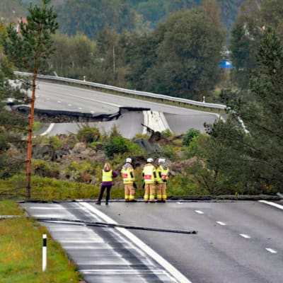 Tre brandmän och en kvinna står och inspekterar en väg som rasat.