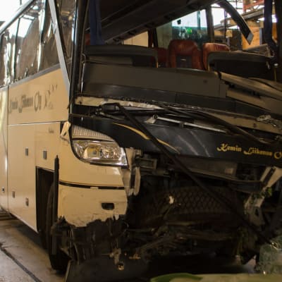 En buss i ett garage.Bussens framparti har omfattande skador. 