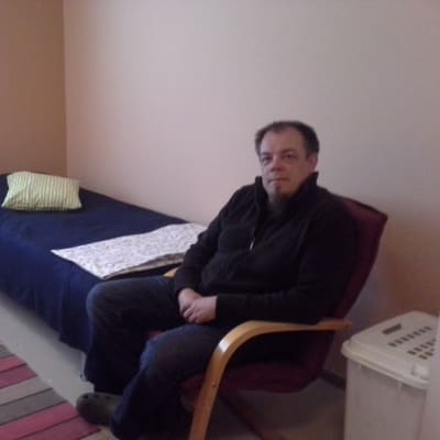 Mies istuu tuolilla nuorisokodin huoneessa sängyn vieressä