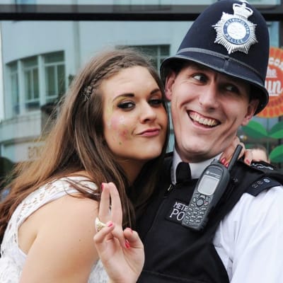 Nuori nainen halaa nauravaa poliisia ja näyttää voitonmerkkiä. 