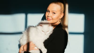 Vaaleahiuksinen hymyilevä nainen pitää sylissään valkoista pitkäkarvaista kissaa.