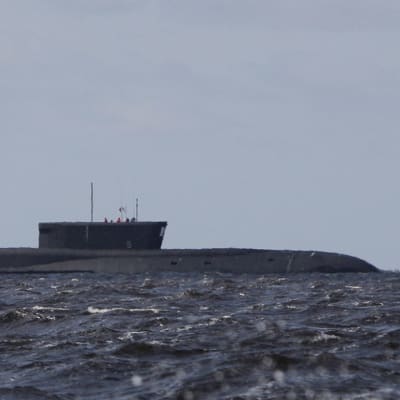 En ubåt ligger i vattnet. I förgrunden syns en motorbåt. Det är sjögång.
