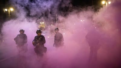Tre kravallutrustade poliser står i ett moln av tårgas