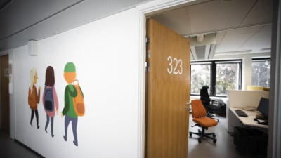 En korridor i ett familjecenter. På den högra sidan en öppen dörr till ett arbetsrum. På vänstra sidan illustrationer på barn på korridorsväggen.