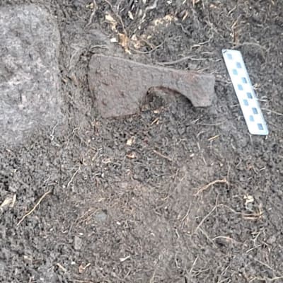 I utgrävningar har man hittat en järnyxa med skaftholk. Intill yxfyndet ligger en mätsticka.