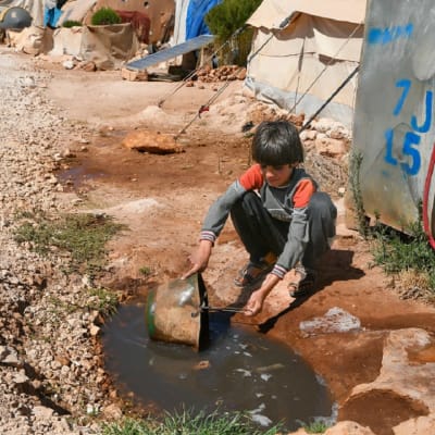 Nuori poika ottaa vettä sankoon kuralätäköstä pakolaisleirillä.